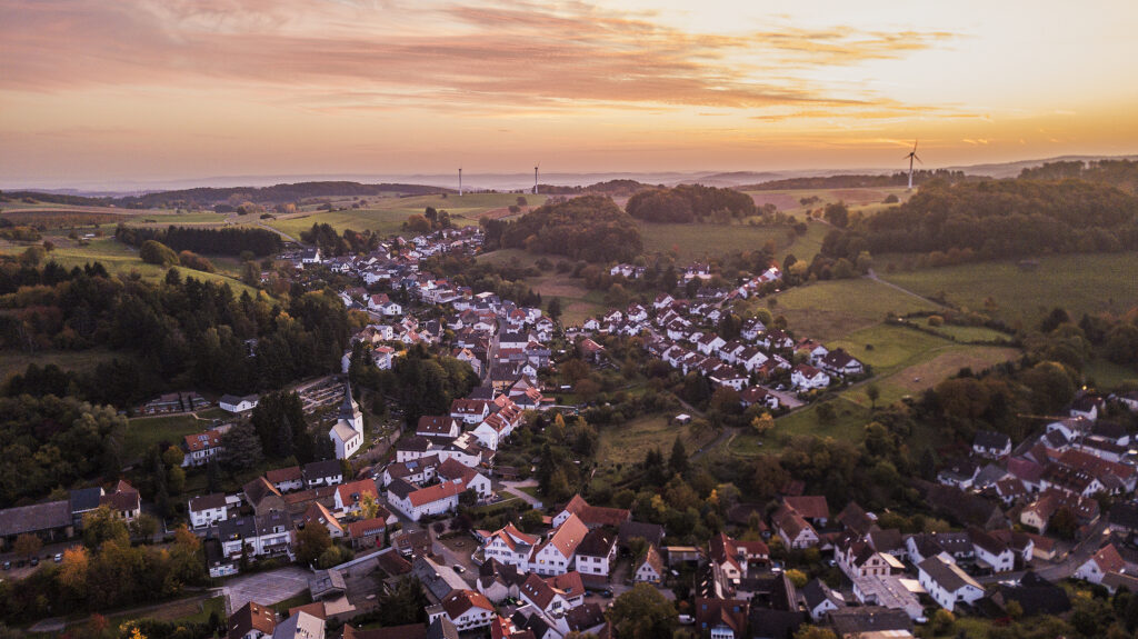 Drohnenaufnahme des Odenwalds, Ober-Beerbach, weiter Blick in der Morgensonne, Windräder sind zu sehen sowie viele Wohnhäuser