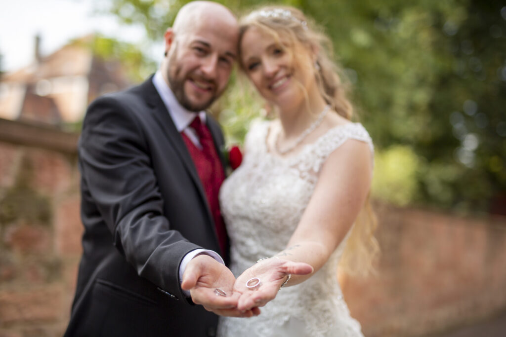 Brautpaar ist unscharf zu sehen, strecken die Hände nach vorne, die Ringe liegen in den Händen