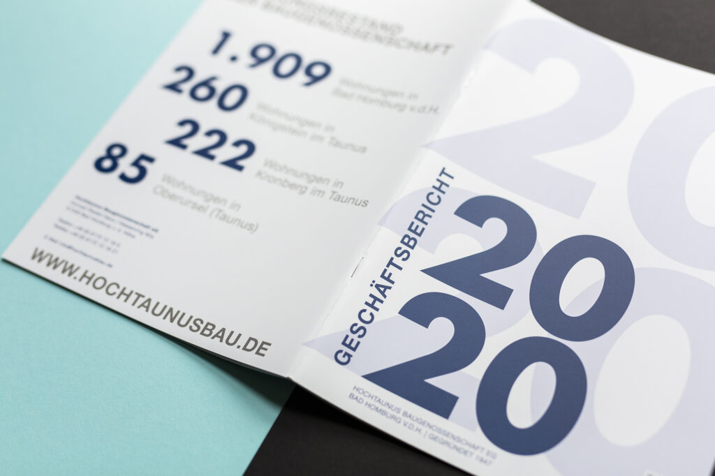 Aufgeschlagener Geschäftsbericht, Umschlag ist komplett zu sehen, fotografiert auf hellblauen und schwarzem Hintergrund